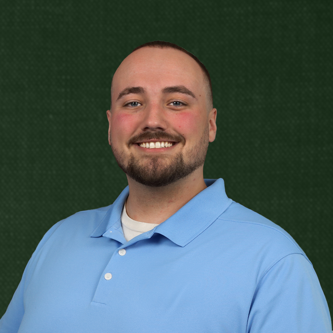 Professional headshot of Nic Rubolino, the founder of Noble Lion Marketing with a friendly smile, and short brown hair, wearing a blue shirt against a green background.